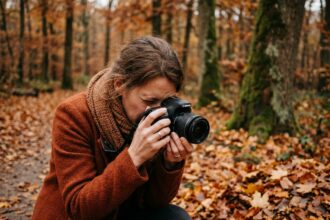 Photographe femme réglant la correction dioptrique de son appareil photo en forêt automnale aux feuilles colorées